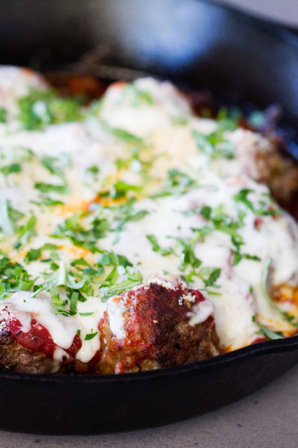 Meatballs and sauce in a skillet topped with melted mozzarella cheese.