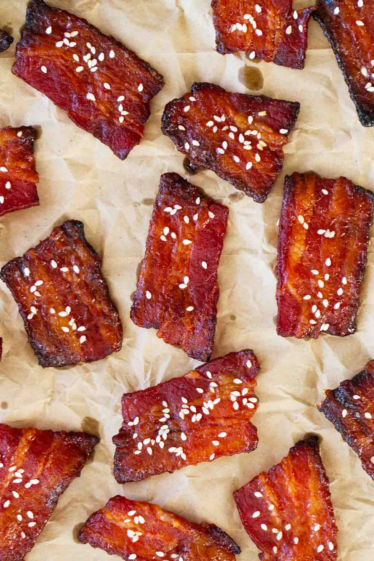 Brown Sugar Sriracha Bacon Bites topped with sesame seeds on a piece of parchment paper.
