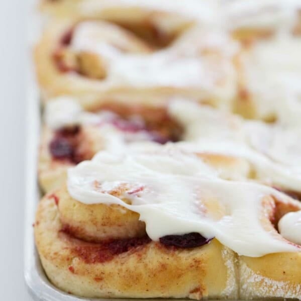 cranberry cinnamon rolls with frosting on a sheet pan