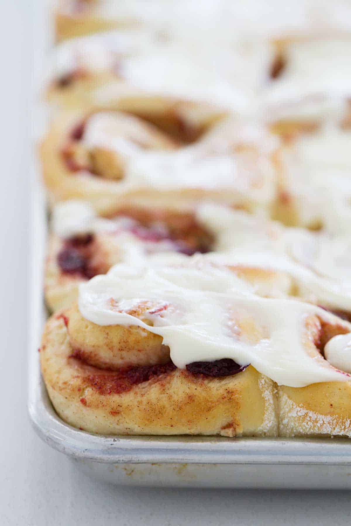 cranberry cinnamon rolls with frosting on a sheet pan