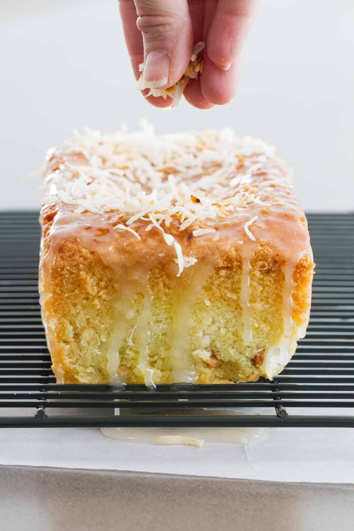 coconut loaf on a cooling rack with coconut being sprinkled over the top