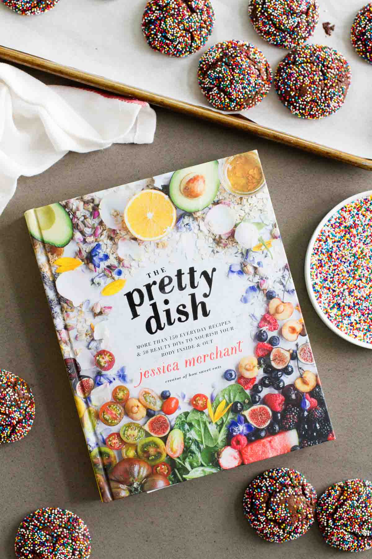 The Pretty Dish cookbook with chocolate crinkle sprinkle cookies and extra sprinkles