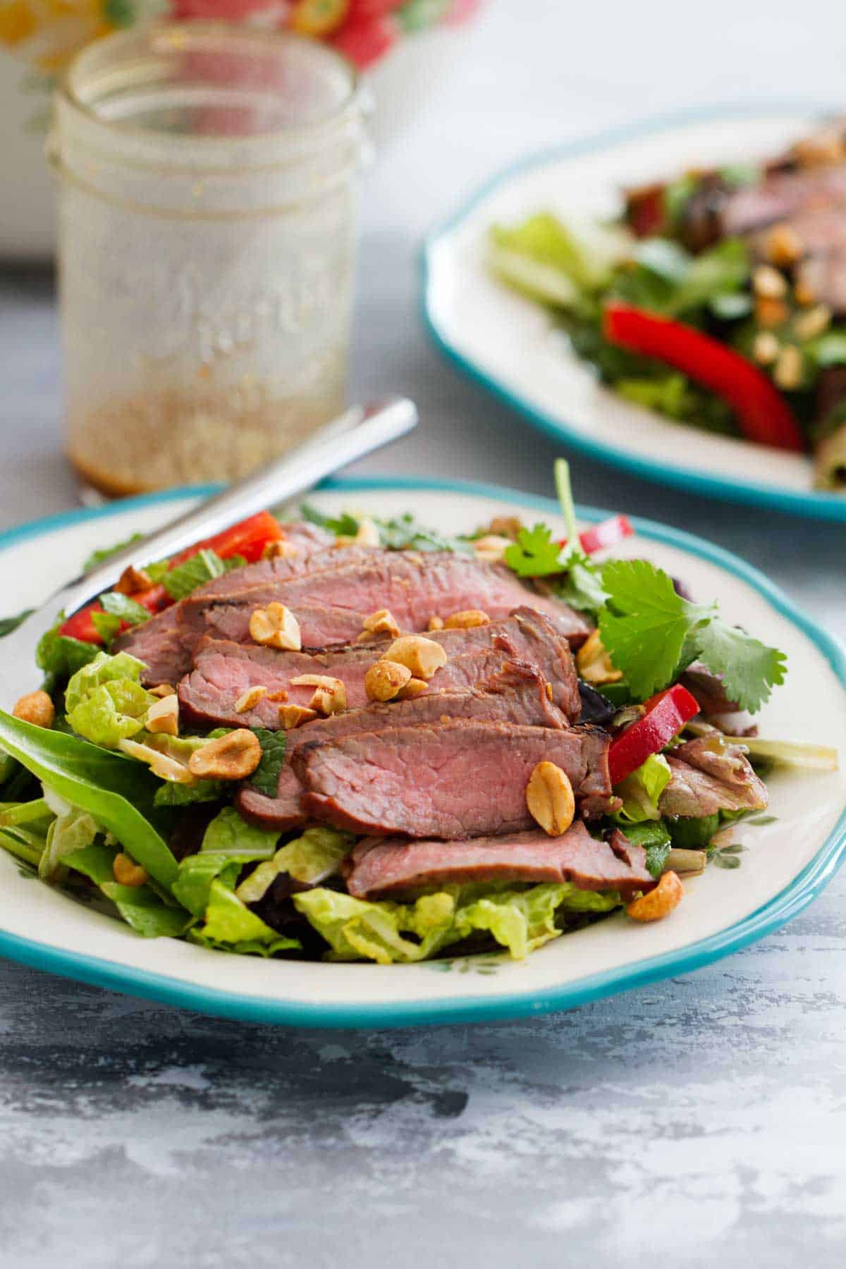 Anything but boring, this Thai Beef Salad is a hearty side dish or easy main dish that you’ll want to serve all summer long. Juicy, flavorful steak goes on this salad filled with lots of vegetables and Thai flavors. Plate with Thai Beef Salad topped with peanuts.