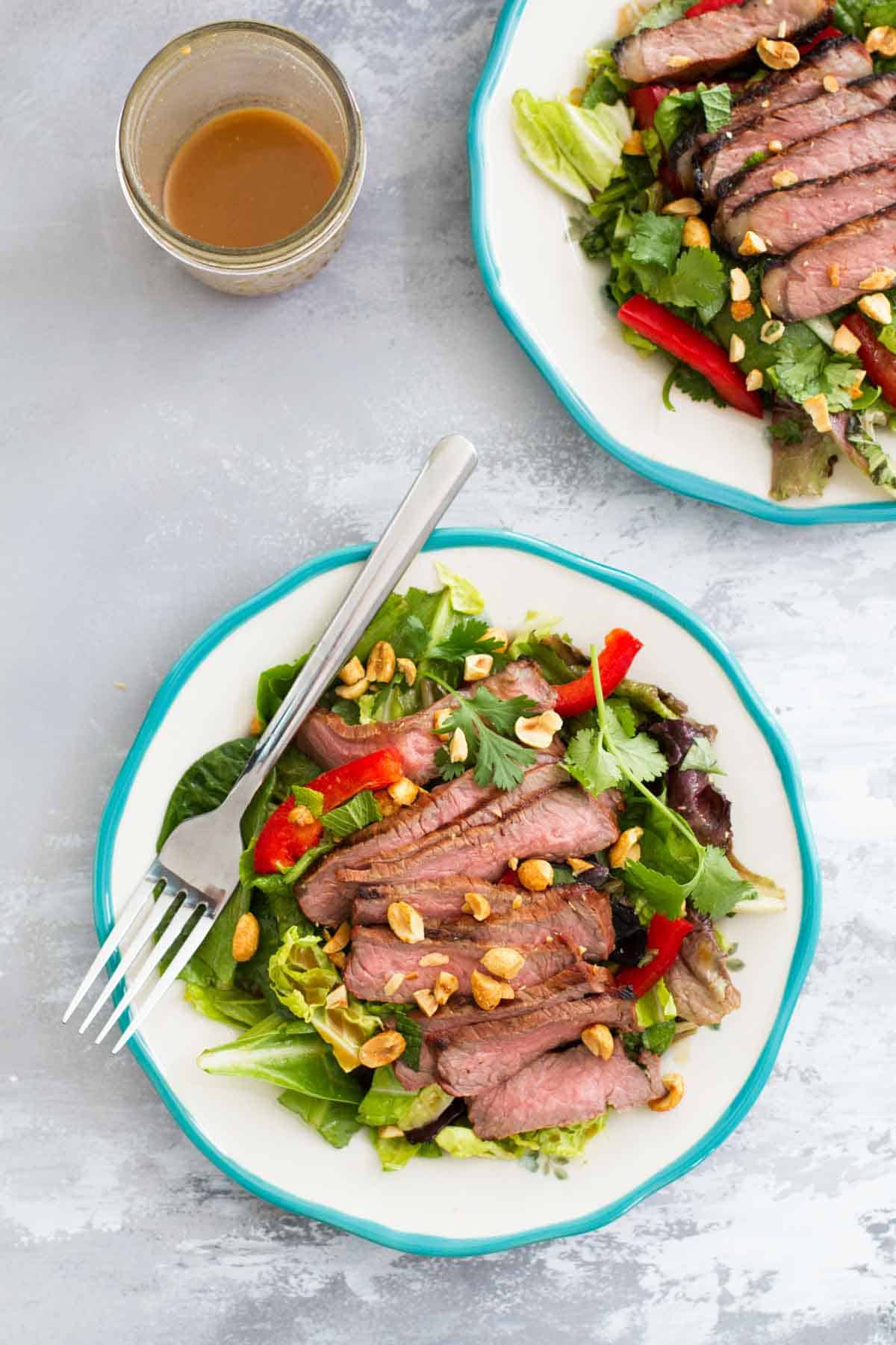 Two plates with Thai beef salad with salad dressing.