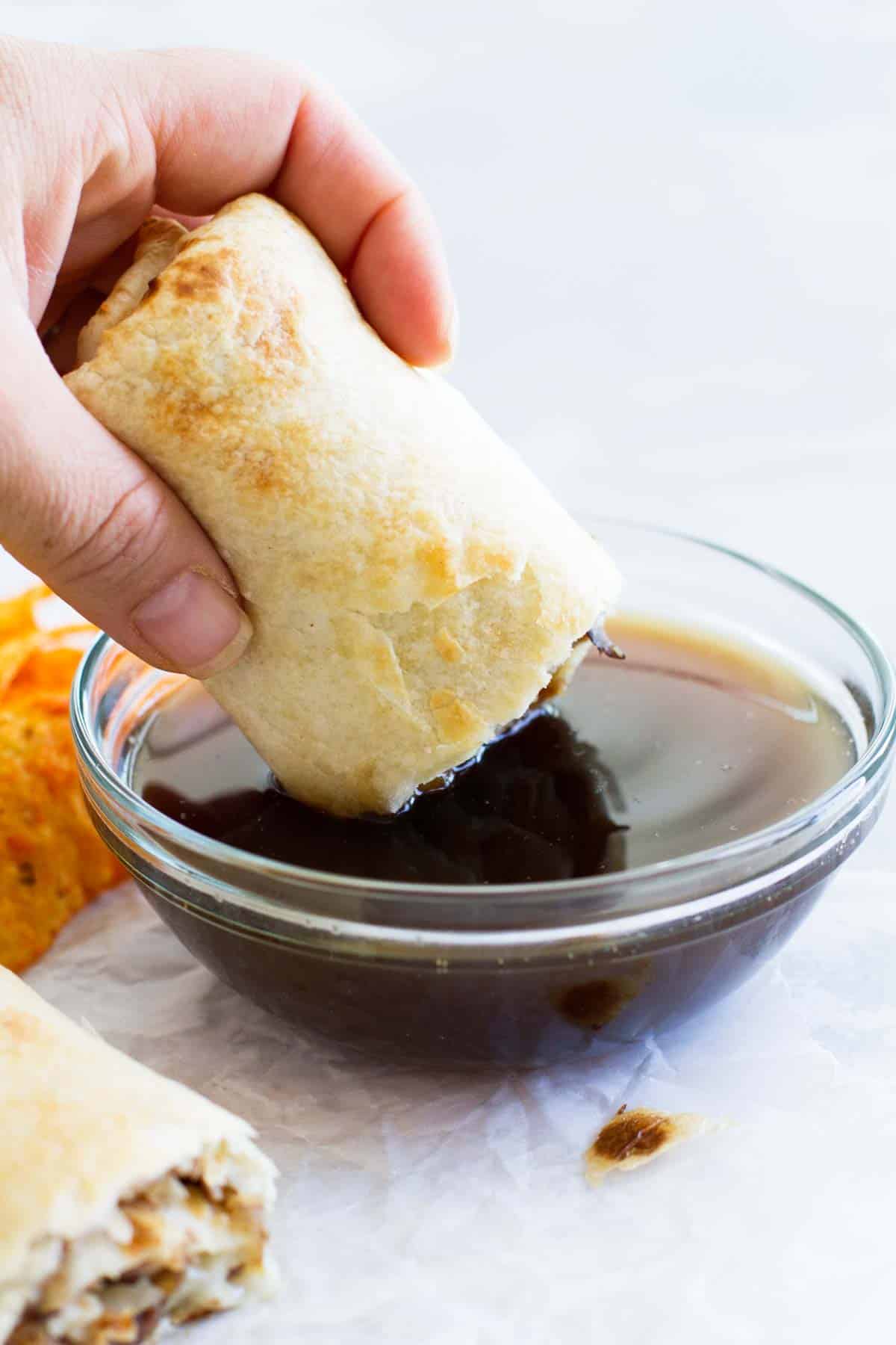 French Dip Tortilla Roll Up being dipped in au jus