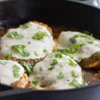 Salsa Verde Chicken topped with cheese in a cast iron skillet.