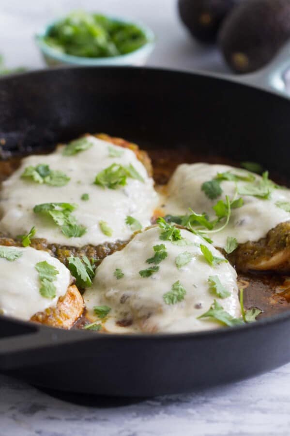 Salsa Verde Chicken topped with cheese in a cast iron skillet.