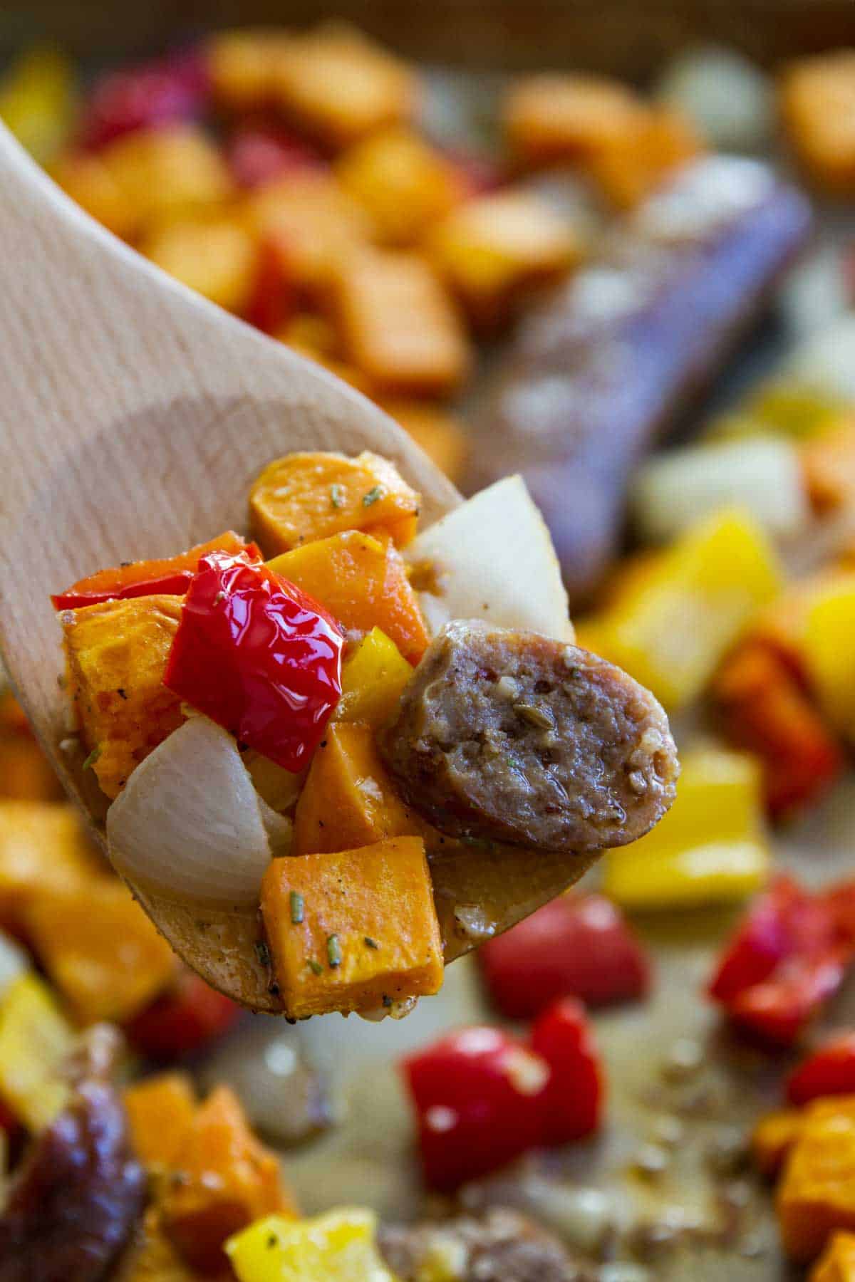 Easy Sheet Pan Dinner - Sausage and Peppers with Sweet potatoes on a wooden spoon