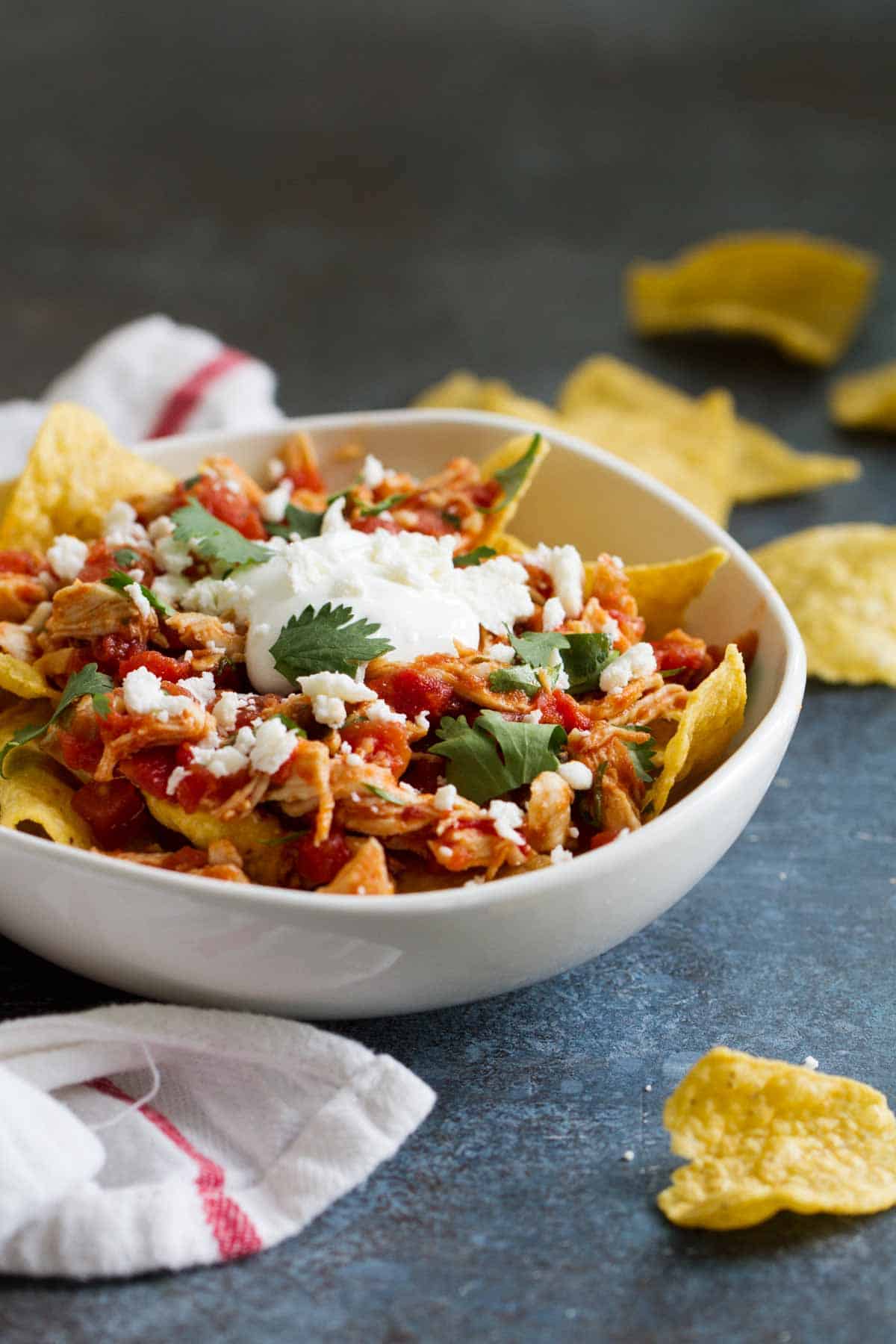 Bowl of chicken chilaquiles topped with sour cream and cheese.