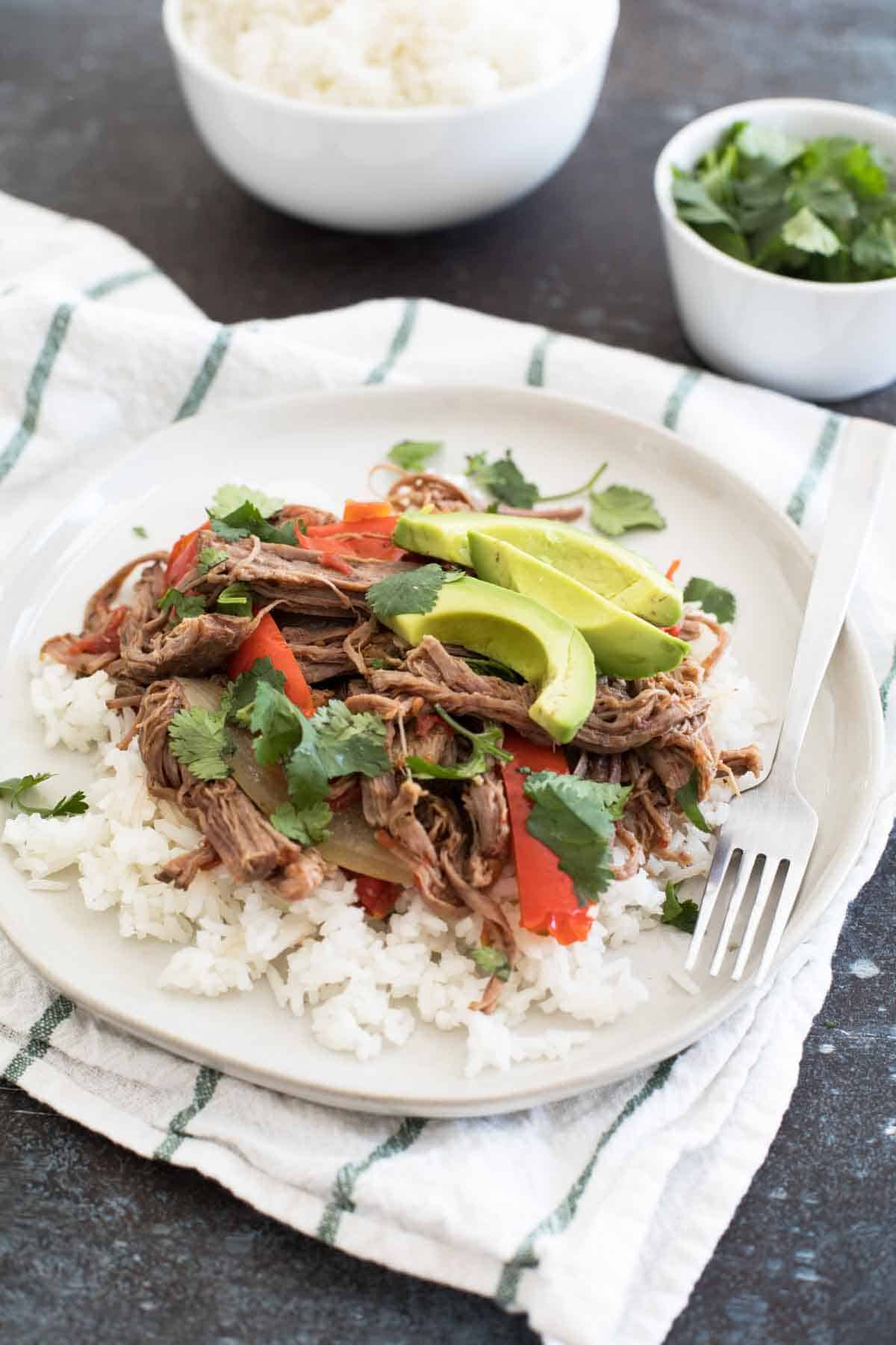 Slow cooker beef served over rice and topped with avocado and cilantro.