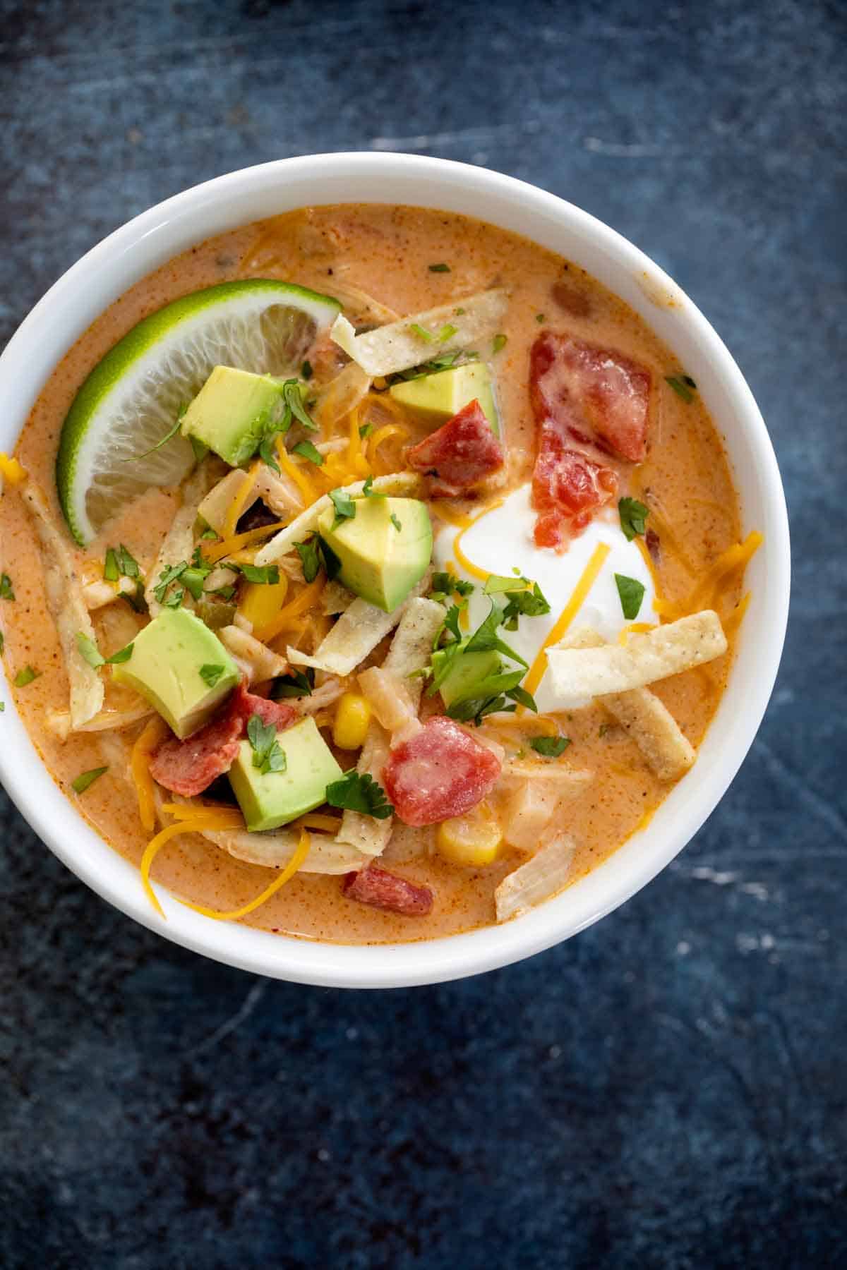 overhead view of bowl of Chicken Tortilla Soup topped with cheese, avocado and tortilla strips