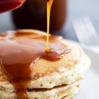 Pouring buttermilk syrup on a stack of pancakes.