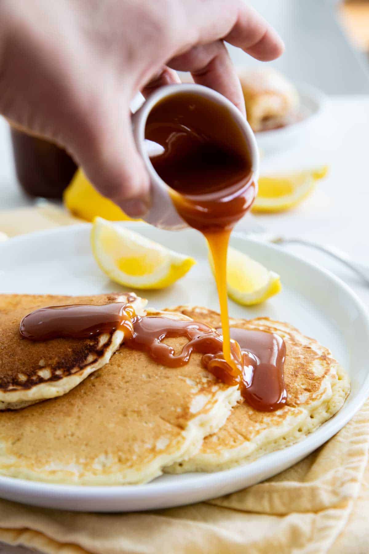 Fluffy and delicious with just the right amount of lemon flavor, these Lemon Pancakes are the perfect breakfast food. Serve them up with Homemade Buttermilk Syrup for a decadent meal that you won’t forget. Lemon Pancakes with Homemade Buttermilk Syrup being poured over the top
