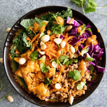 Overhead view of a buddha bowl with farro, chicken, sauce, and other ingredients.