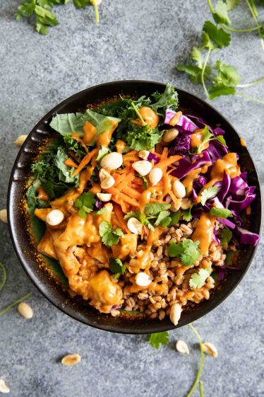 Overhead view of a buddha bowl with farro, chicken, sauce, and other ingredients.