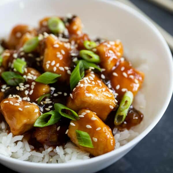 bowl filled with general tso chicken topped with sesame seeds and green onions