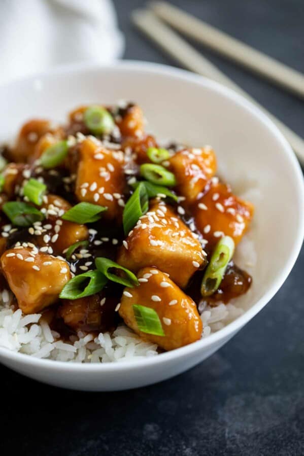 bowl filled with general tso chicken topped with sesame seeds and green onions