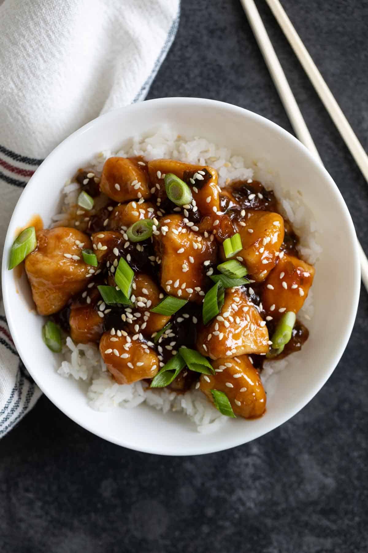 overhead view of a bowl of rice topped with general tso chicken and green onions