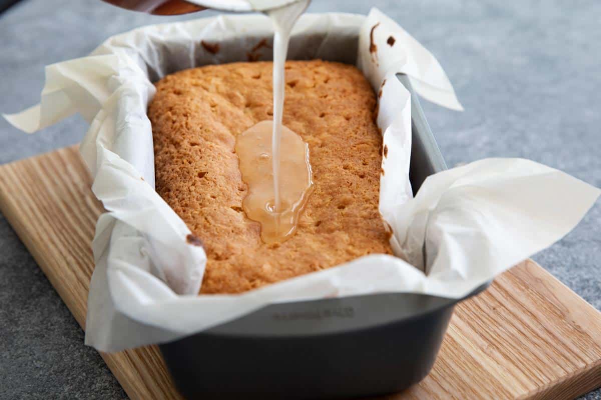 pouring coconut glaze on a quick bread