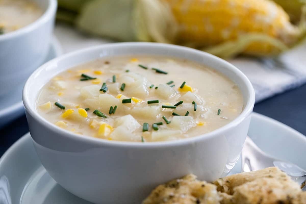 A perfect way to use up bountiful fresh corn, this Potato Corn Chowder is the perfect end of summer soup. Or freeze extra grilled corn for a delicious soup all winter long. Bowl of Potato Corn Chowder with corn in the background