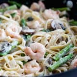Shrimp alfredo with mushrooms and asparagus in a skillet.
