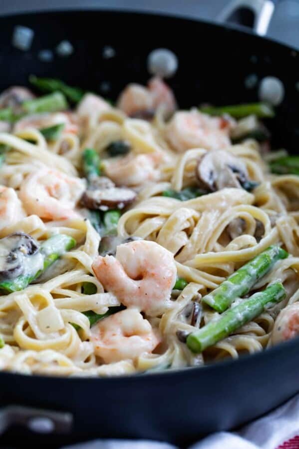 Shrimp alfredo with mushrooms and asparagus in a skillet.