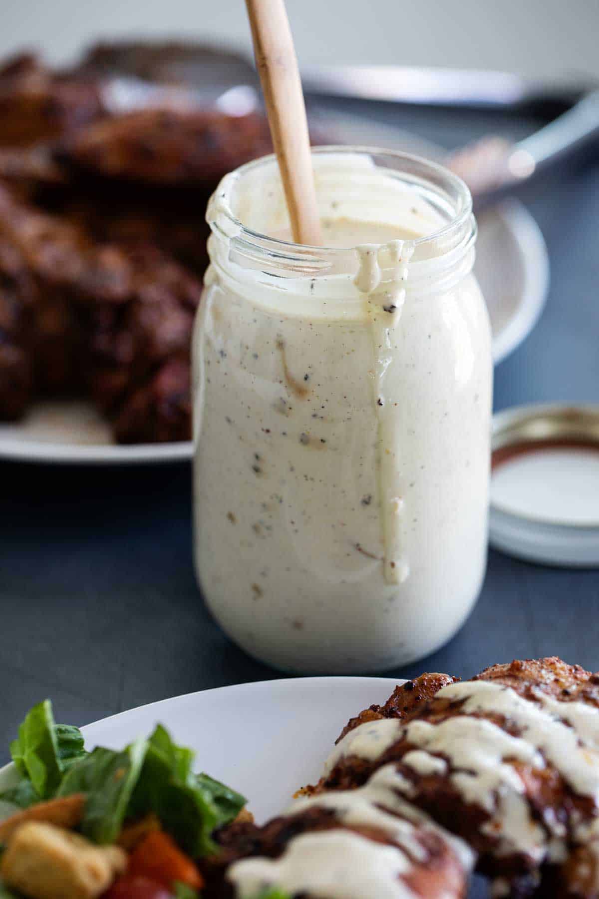 Alabama White Sauce in a jar with chicken on a plate.