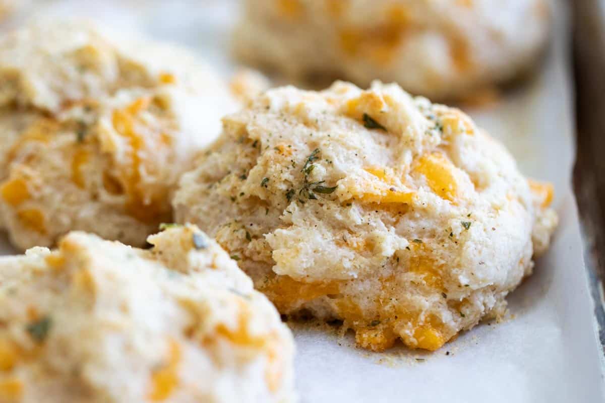 If you love the Red Lobster biscuits, you’ll go love these Red Lobster Cheddar Biscuits! Filled with herbs and garlic, these tender biscuits are a great copycat recipe that belong on your dinner table. Copycat Red Lobster Cheddar Biscuits on a baking sheet lined with parchment paper.