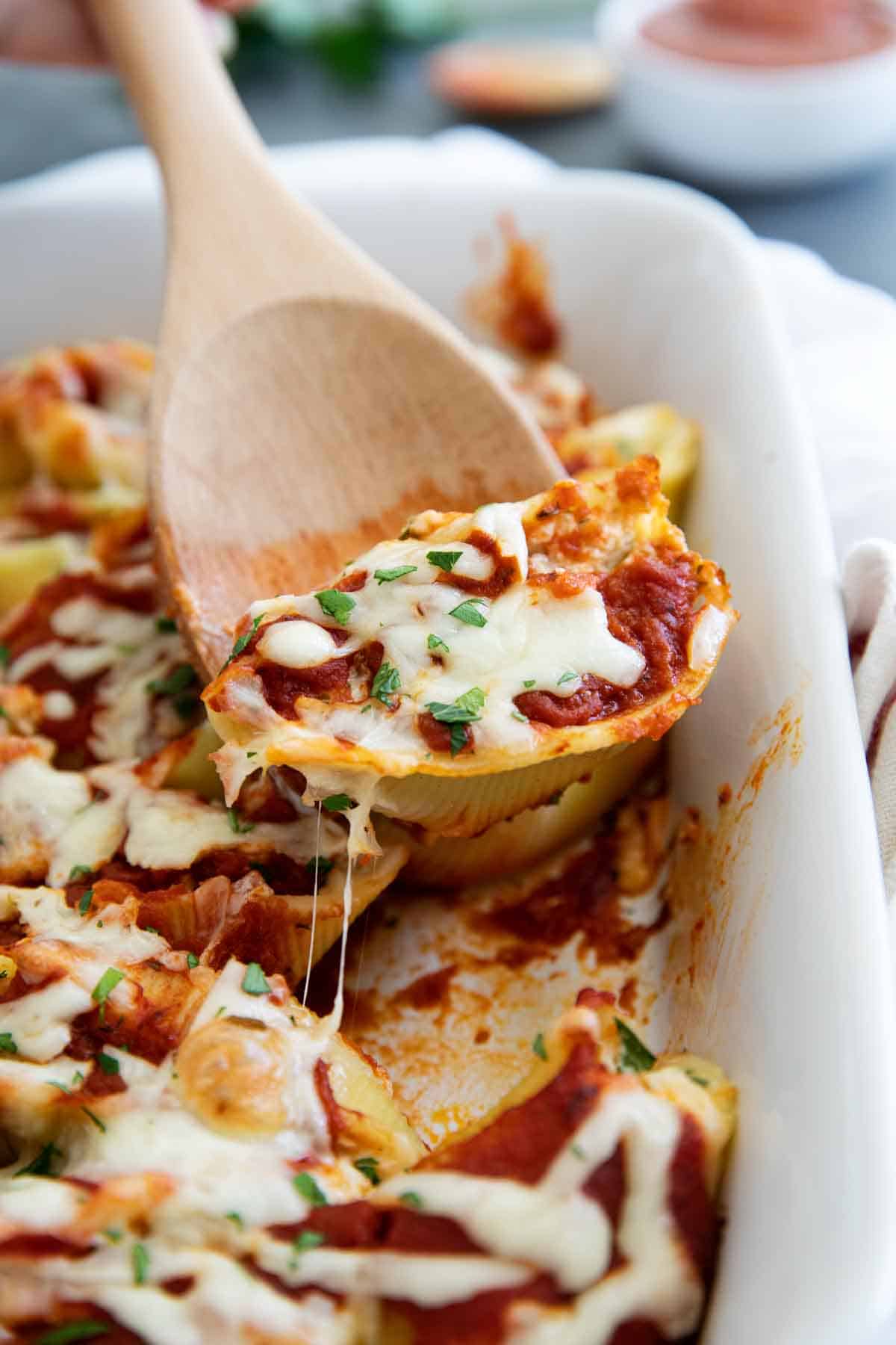 Stuffed Shell in baking dish with wooden spoon scooping out