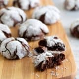 cutting board with chocolate crinkle cookies, with one cookie broken into pieces.