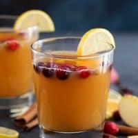 Hot Apple Cider in glasses with cranberries floating on top.
