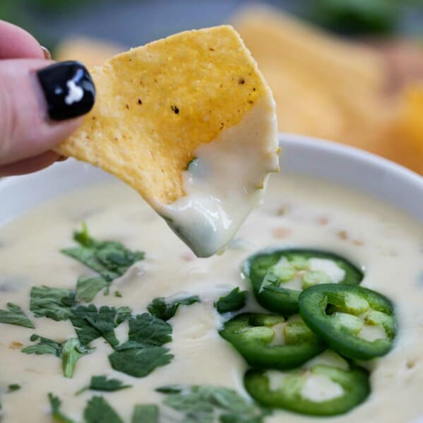 chip being dipped into creamy white queso dip