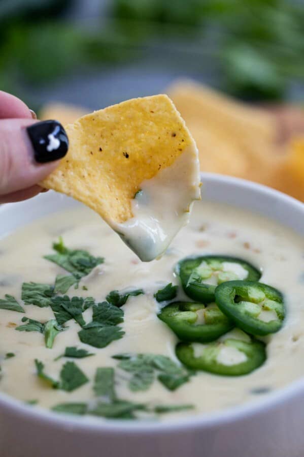 chip being dipped into creamy white queso dip