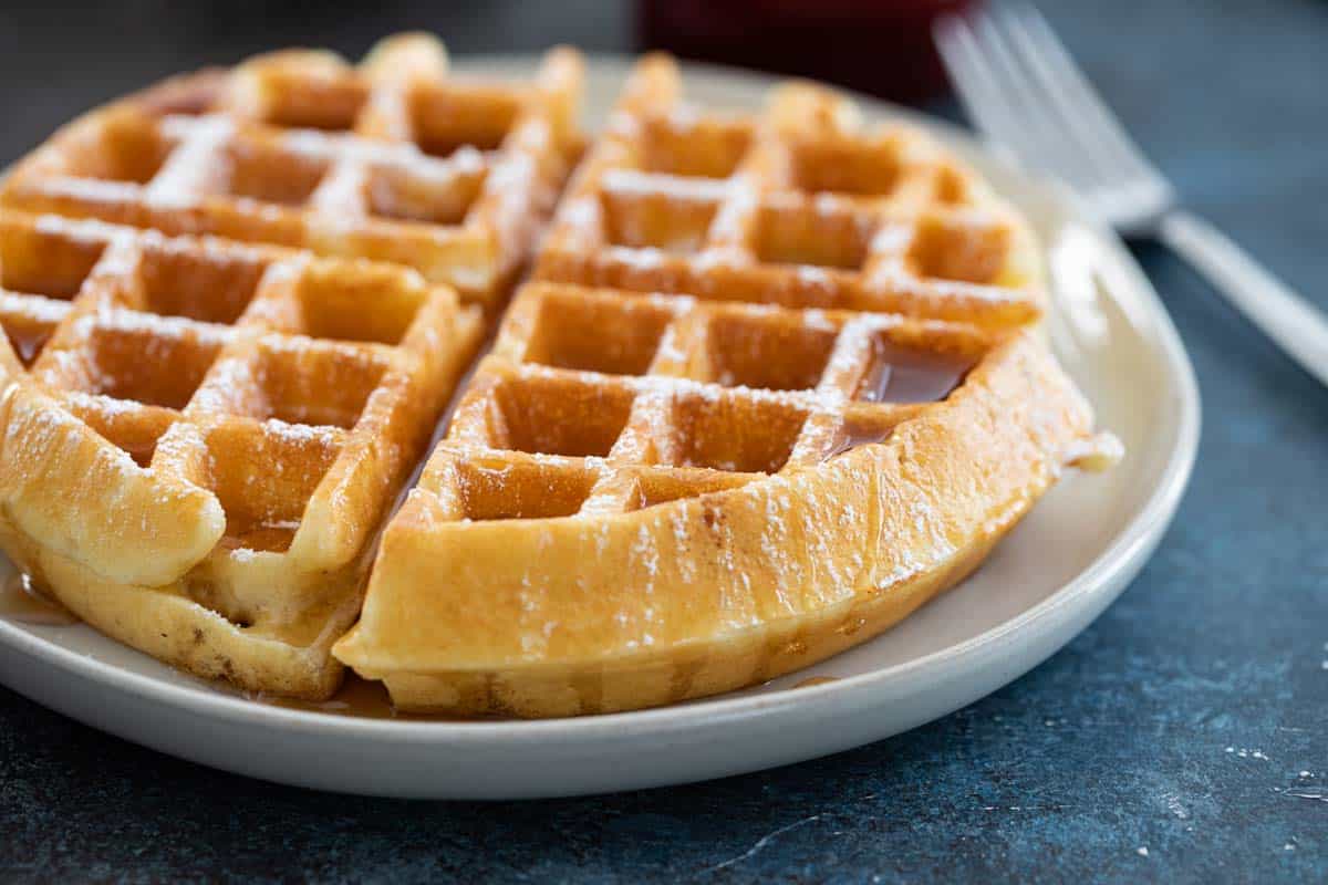 waffle on a plate with syrup and powdered sugar