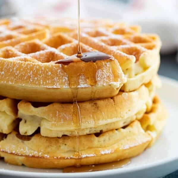 pouring syrup on a stack of waffles