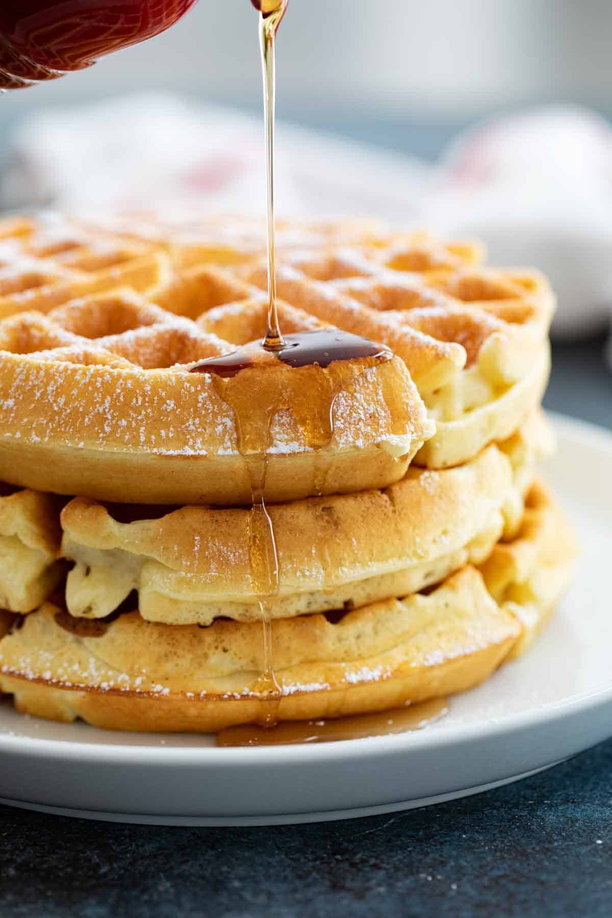 pouring syrup on a stack of waffles