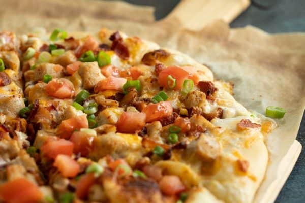 Pizza topped with chicken, bacon, ranch, tomatoes and green onions