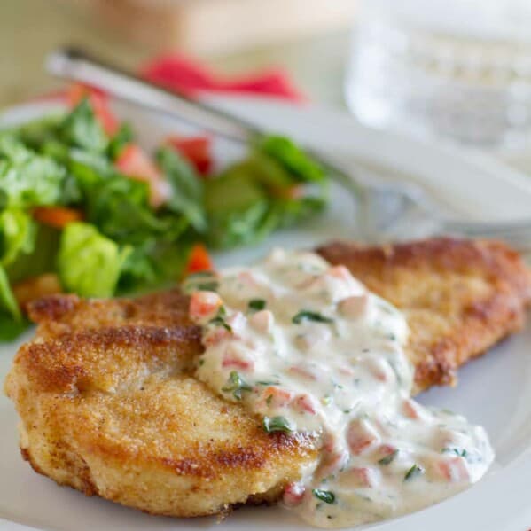 crispy chicken served with basil cream sauce with a salad in the background