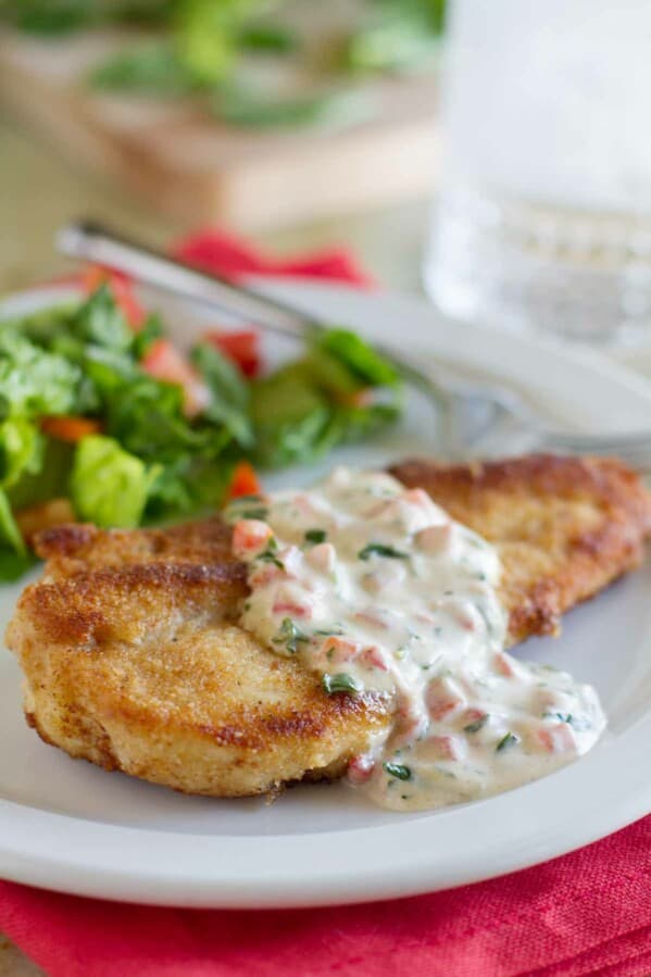 crispy chicken served with basil cream sauce with a salad in the background