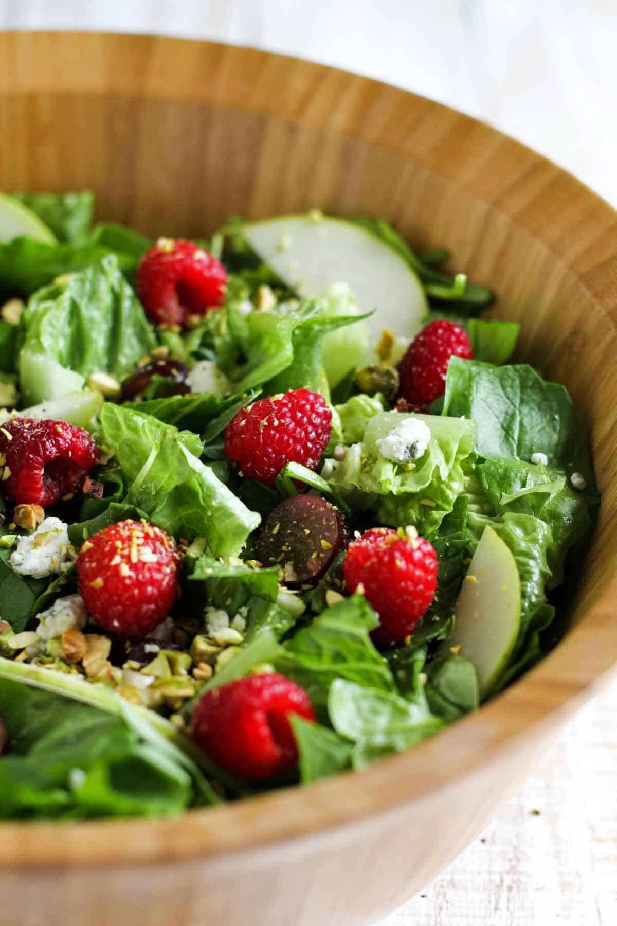 This Raspberry Spinach Salad has spinach, romaine, grapes, dried cranberries, pear, raspberries, blue cheese and pistachios and is served with a homemade raspberry vinaigrette. Red Raspberry Spinach Salad with Raspberry Vinaigrette in a wooden bowl.