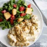 Poppy Seed Chicken with a salad on a white plate with a fork on the side