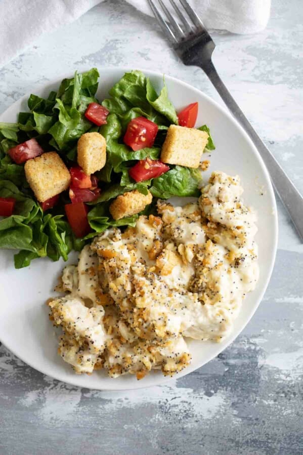 Poppy Seed Chicken with a salad on a white plate with a fork on the side