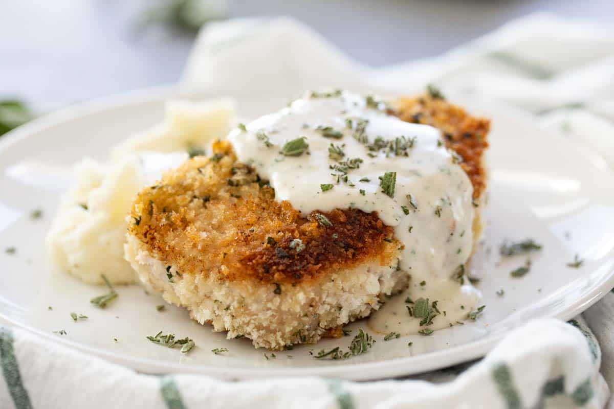 Breaded Pork Chops with Cream Gravy Recipe - Breaded pork chops are combined with cream gravy with parsley and sage for a delicious, easy and quick dinner full of flavor. breaded pork chop with cream gravy on a plate