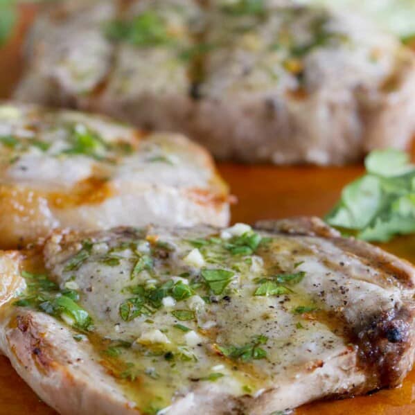 grilled pork chops with a cilantro and lime sauce on a cutting board