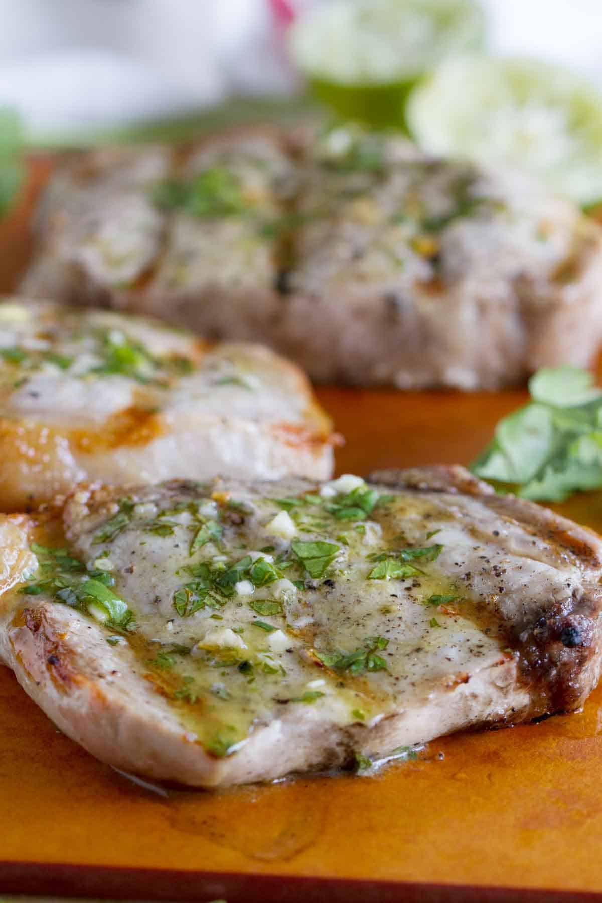 grilled pork chops with a cilantro and lime sauce on a cutting board