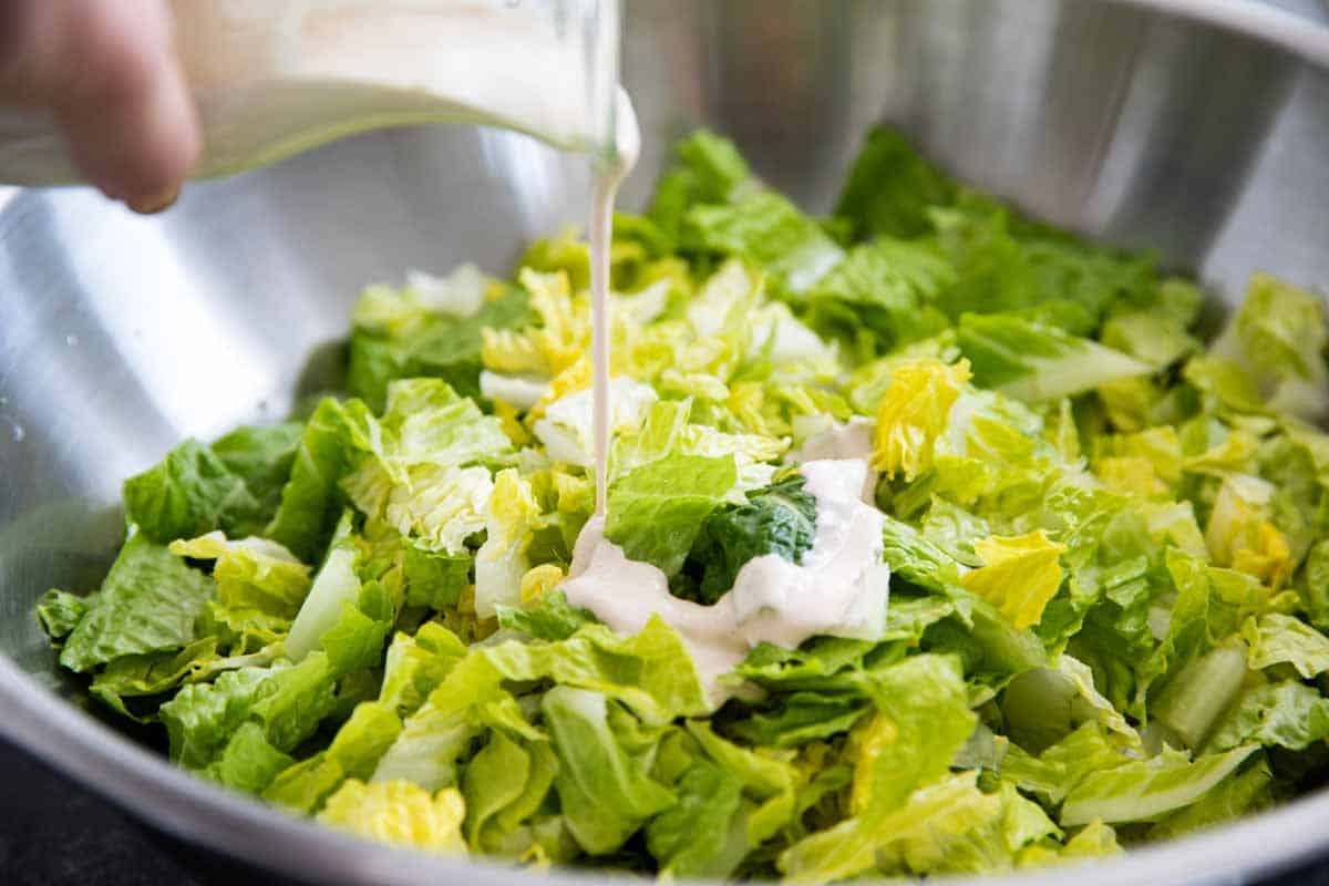 pouring Caesar dressing over greens