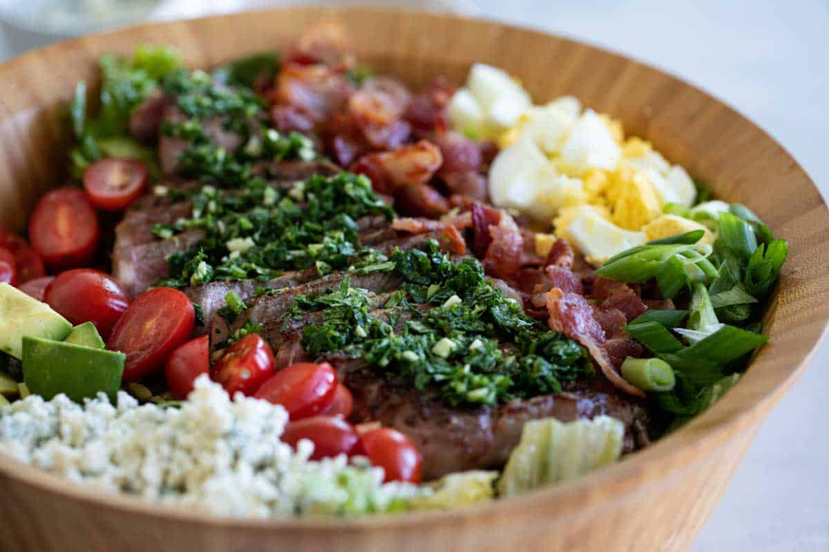 Turn your salad into a meal with this Steak Cobb Salad. All of your favorite Cobb Salad ingredients plus steak on top to turn it into a hearty meal. Cobb Salad with Steak in a wooden bowl.