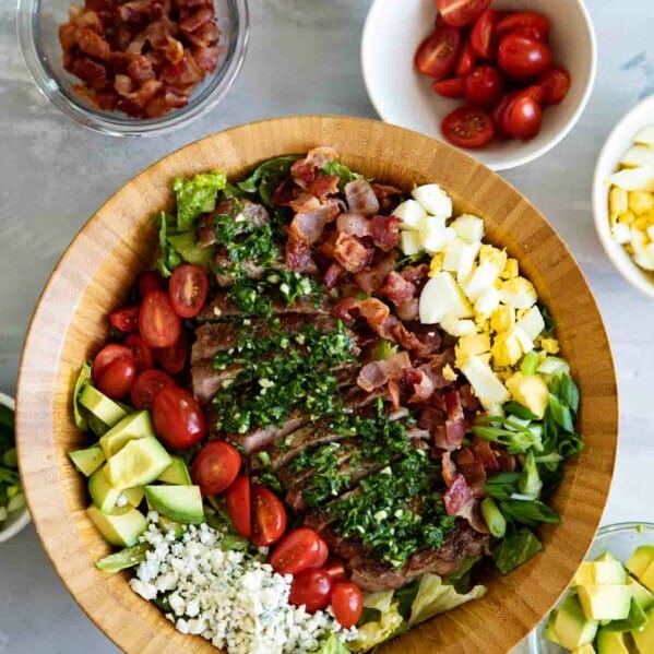 top view of steak cobb salad with bowls of ingredients on the side