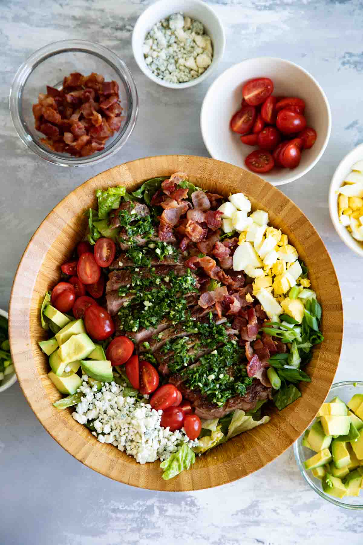 top view of steak cobb salad with bowls of ingredients on the side