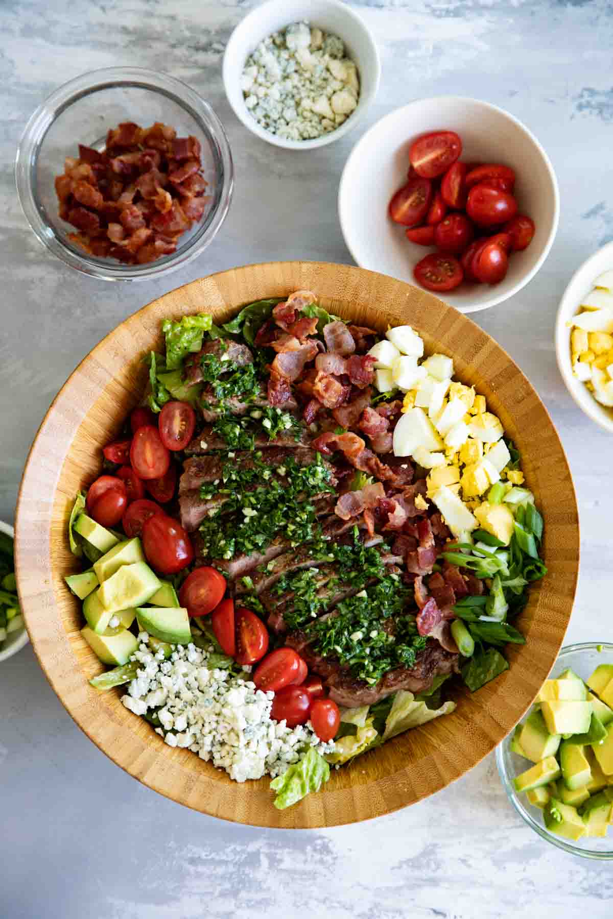 Turn your salad into a meal with this Steak Cobb Salad. All of your favorite Cobb Salad ingredients plus steak on top to turn it into a hearty meal. top view of steak cobb salad with bowls of ingredients on the side